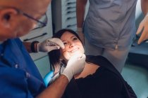 Dentista y enfermera dental que realiza procedimiento dental en paciente femenino - foto de stock