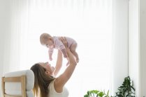 Mother lifting baby girl up in living room — Stock Photo