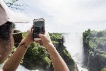 Vue arrière de jeune touriste femme faisant des photos avec smartphone de Victoria Falls, Zimbabwe, Afrique — Photo de stock