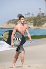 Молодий чоловік, що перевозять дошку для серфінгу на пляжі — стокове фото