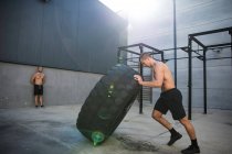Man exercising in gymnasium, lifting tire — Stock Photo