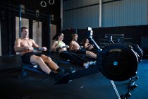 Group of people exercising in gymnasium, using rowing machines — Stock Photo