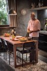 Uomo maturo al tavolo da cucina peeling frutta in ciotola — Foto stock