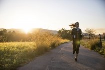 Jovem mulher correndo ao longo da estrada rural — Fotografia de Stock