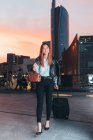 Businesswoman walking outdoors with wheeled suitcase at sunset — Stock Photo