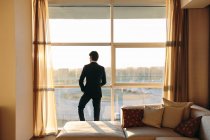 Бизнесмен, выглядывающий из окна спальни отеля — стоковое фото