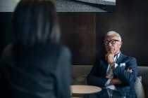 Homme d'affaires senior assis à la table de l'hôtel réunion avec une femme d'affaires, vue sur l'épaule — Photo de stock