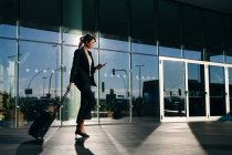 Businesswoman with wheeled luggage passing glass building, Malpensa, Milan — Stock Photo