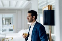 Businessman with iced drink, deep in thoughts in suite — Stock Photo