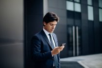 Uomo d'affari che utilizza lo smartphone di fronte all'edificio per uffici — Foto stock