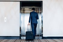Empresário com bagagem de rodas entrando elevador do hotel — Fotografia de Stock