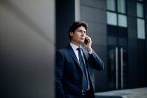 Businessman using smartphone in front of office building — Stock Photo