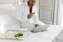 Man using laptop and having toast in suite — Stock Photo