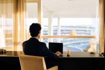 Geschäftsmann benutzt Laptop und schaut aus Hotelschlafzimmerfenster — Stockfoto