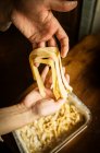 Hohe Nahaufnahme einer Person, die frisch zubereitete Tagliatelle-Pasta in ein Metallblech legt. — Stockfoto