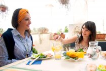 Женщина и девушка с длинными каштановыми волосами сидят за столом, наливая стакан апельсинового сока. — стоковое фото