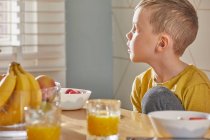 Boy sitting at breakfast table, looking out of window. — Stock Photo
