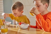 Two boys sitting at kitchen table, eating breakfast. — Stock Photo