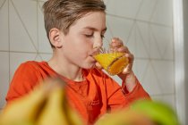 Хлопчик сидить за столом, п'є апельсиновий сік . — стокове фото