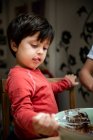 Young boy with black hair sitting at a kitchen table, baking chocolate cake. — Stock Photo