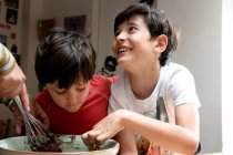 Два мальчика с черными волосами сидят за кухонным столом и пекут шоколадный торт.. — стоковое фото