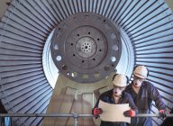 Two engineers standing in front of low pressure steam turbines for electricity generation in turbine repair factory. — Stock Photo