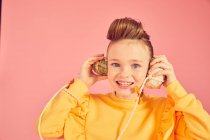 Ritratto di ragazza bruna che indossa la parte superiore gialla, che tiene il telefono con guscio di mare, su sfondo rosa, guardando la macchina fotografica — Foto stock