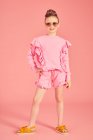 Comprimento total, menina morena vestindo top babados rosa com shorts, usando óculos de sol no fundo rosa e posando na câmera, mão sobre quadril — Fotografia de Stock