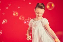 Мила дівчина в романтичній білій сукні на червоному тлі, оточена мильними бульбашками — стокове фото