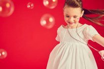 Брюнетка дівчина в романтичній білій сукні на червоному тлі, оточена мильними бульбашками — стокове фото