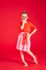 Brunette girl wearing in sunglasses and skirt, posing and standing on red background — Stock Photo