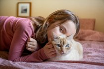 Porträt eines Mädchens und einer weißen Ingwerkatze, die auf dem Bett liegt. — Stockfoto