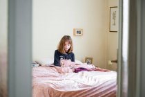 Chica sentada en su cama en su habitación, estudiando, la educación en casa con el ordenador portátil y portátil - foto de stock