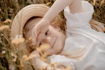 Portrait de jeune fille aux cheveux blonds portant un chapeau de paille, couché dans une prairie. — Photo de stock