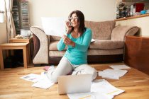 Frau sitzt auf Holzboden im Wohnzimmer, umgeben von Laptop und Papieren, arbeitet während der Coronavirus-Krise von zu Hause aus. — Stockfoto