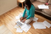 Woman sitting on wooden floor in living room, surrounded by laptop and papers, working from home during Coronavirus crisis. — Stock Photo