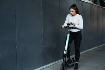 Mujer joven con el pelo castaño largo de pie en scooter eléctrico. - foto de stock