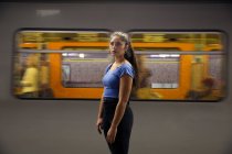 Mujer joven con el pelo castaño largo de pie delante del tren de cercanías en la plataforma de la estación de tren. - foto de stock