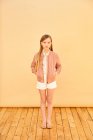Портрет дівчини з довгим світлим волоссям у шортах, сорочці та рожевій куртці на блідо-жовтому тлі . — стокове фото