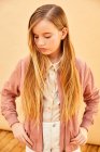 Ritratto di ragazza con lunghi capelli biondi che indossa pantaloncini, camicia e giacca rosa, su sfondo giallo pallido. — Foto stock