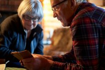 Пожилая пара сидит за столом в бревенчатой хижине, смотрит на мобильный телефон, Vasterbottens Lan, Швеция. — стоковое фото