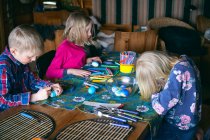 Boy and two girls sitting at a table in a log cabin, doing handicrafts, Vasterbottens Lan, Sweden. — Stock Photo