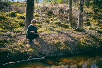 Boy kneeling on riverbank in a forest in Vasterbottens Lan, Sweden. — Stock Photo