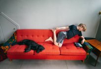 Aus der Vogelperspektive: Junge und schwarzer Hund liegen auf rotem Sofa, Vasterbottens Lan, Schweden. — Stockfoto
