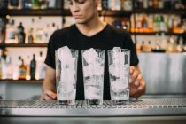 Young man wearing black clothes standing behind bar counter, preparing drinks. — Stock Photo