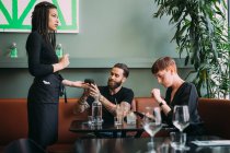 Young woman with short hair and bearded young man sitting in a bar, using mobile phone to pay. — Stock Photo