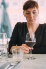 Молода жінка з коротким волоссям у чорному верхньому одязі сидить за столом у барі, п'є червоне вино . — стокове фото