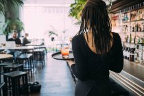 Вид сзади на официантку в черной одежде, работающую в баре, несущую напитки на подносе. — стоковое фото