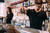 Jeune femme et homme portant des vêtements noirs debout derrière le comptoir du bar, préparant des boissons. — Photo de stock