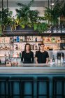 Portrait of young woman and man wearing black clothes standing behind bar counter, smiling at camera. — Stock Photo